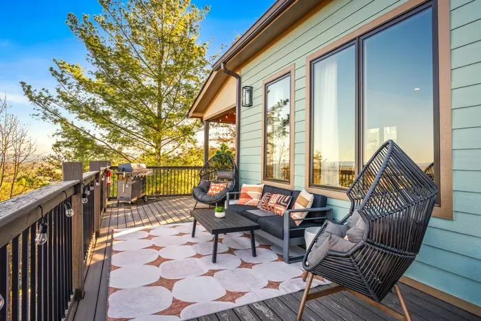 Whole crew spreads across the covered deck. Sectional, egg chairs, grill standing by at one end. The outdoor living room where the whole weekend ends up parked from morning to late.