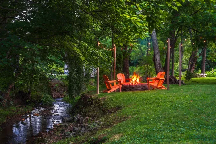 Creekside fire pit oasis with string lights and wooded charm