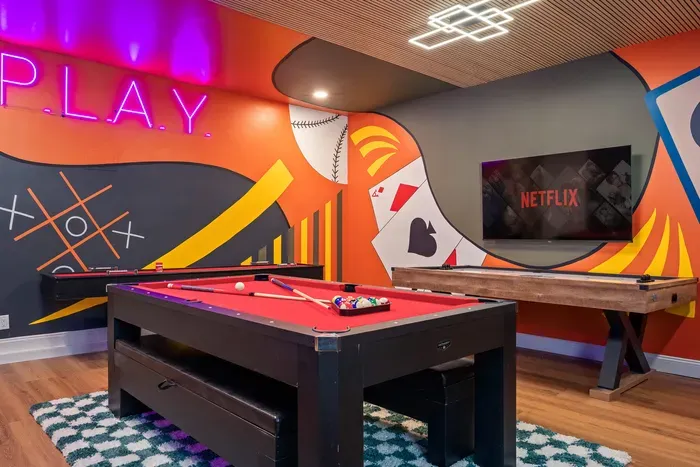 Stylish game room with pool, shuffleboard, neon art, and big-screen TV