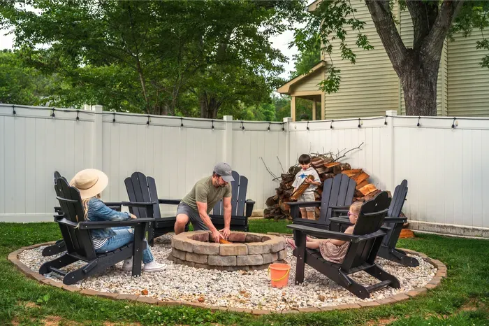 Cozy fenced backyard fire pit with Adirondack seating and string lights