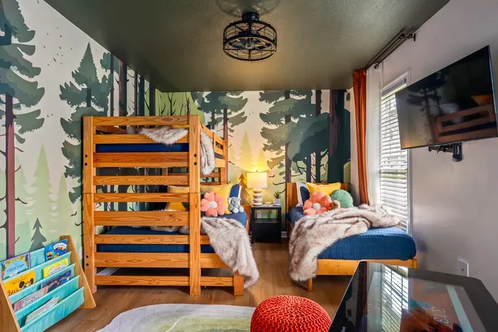 Whimsical forest-themed kids’ room with bunk beds, TV, and cozy touches