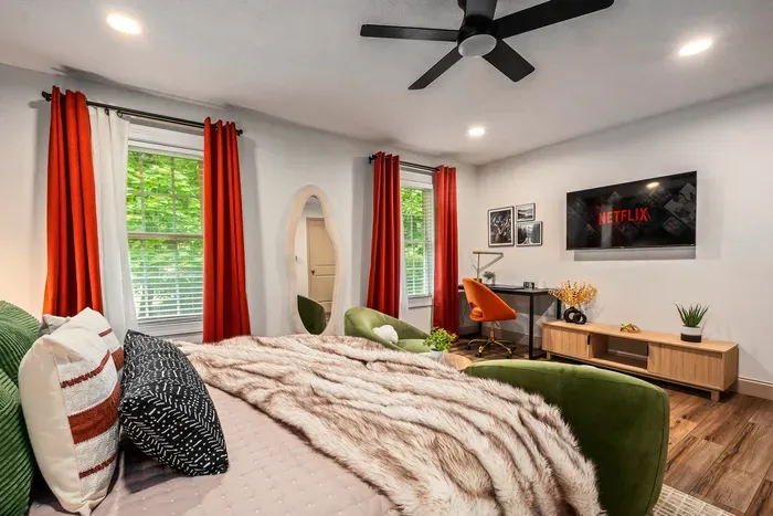 Stylish bedroom with workspace, TV, and bright windows with leafy views
