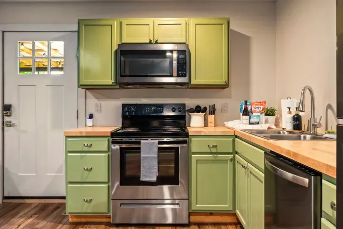 Bright kitchen with green cabinets, butcher-block counters & stainless appliances