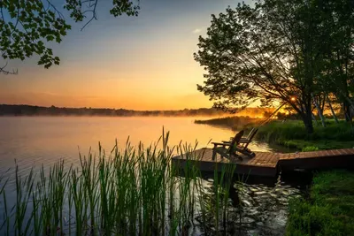 Peaceful lakefront backyard with private dock and Adirondack seating — the perfect spot to enjoy sunrise or sunset views over the water.