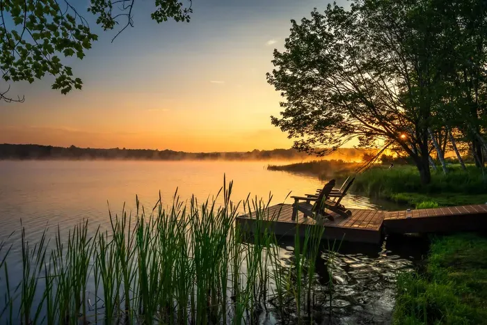 Peaceful lakefront backyard with private dock and Adirondack seating — the perfect spot to enjoy sunrise or sunset views over the water.