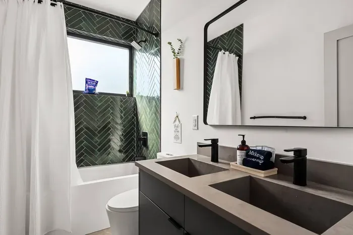 Main floor en suite full bathroom featuring a double vanity with modern black fixtures and a tub/shower combo with bold tile surround—all step-free accessible for added convenience.