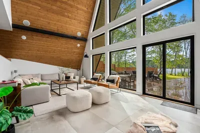 Spacious living room with floor-to-ceiling A-frame windows, stunning lake views, radiant heated floors, Sonos surround sound, and a cozy fireplace.