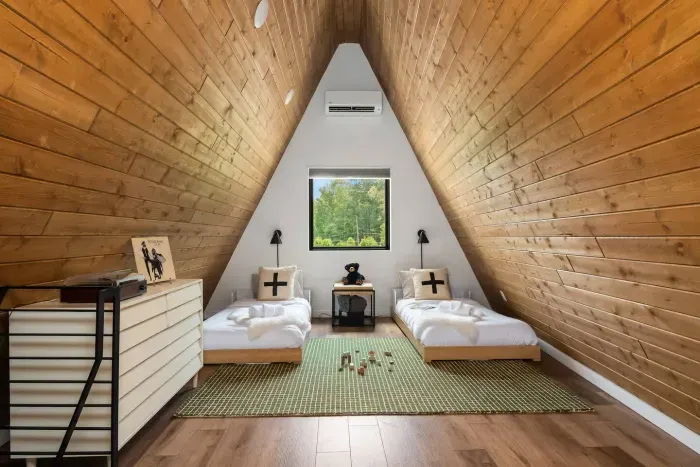 A cozy A-frame retreat with two twin beds, wood-paneled ceilings, and a central window overlooking the trees. Perfect for kids, teens, or friends—this flexible sleeping space makes it easy to accommodate your group’s needs.