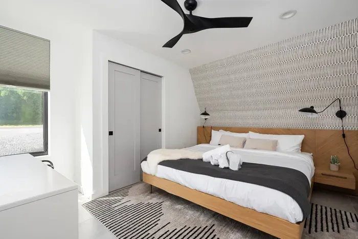 Main floor bedroom with step-free access, heated floors, and a king-size bed dressed in luxury linens. Designed for comfort with blackout shades and a ceiling fan.