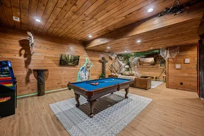 Game room with a full-size pool table, arcade cabinet, and hand-painted forest walls. This is the lower level where the tournament runs past midnight.