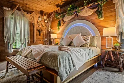 Arched glow-lit headboard, king bed, and drapes framing the woods. This is the room guests photograph before they've even unpacked.