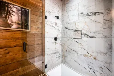 Marble-veined shower surround with matte black fittings. A spa-level finish tucked inside a pine-walled cabin.