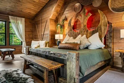 King bed built from raw timber with a live-edge slab headboard. Heavy quilts, quiet nights, mountain air through the window.