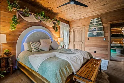 King bed beneath a softly lit arch, wrapped in pine and greenery. The windows open to nothing but trees.