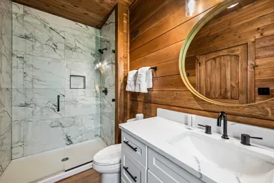 Marble-tiled tub and shower beneath a round mirror. A guest bath that clearly wasn't an afterthought.