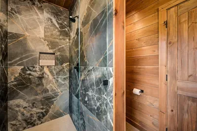 Marble-look walk-in shower with a rainfall head and frameless glass. The shower that makes the drive up worth it.