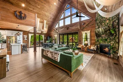 Soaring vaulted ceilings, a stone fireplace, and a two-story wall of windows framing nothing but forest. This is where the whole group ends up every single night.