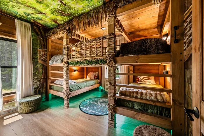 Treehouse bunk room with hand-built log bunks and glowing green floors. The kids will ask when you're coming back before you've finished checking out.