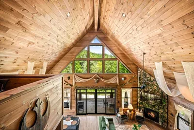 A two-story window wall under a vaulted pine ceiling, fireplace glowing below. Morning light pours through this room before anyone in the house is awake.