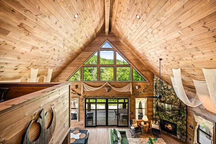 A two-story window wall under a vaulted pine ceiling, fireplace glowing below. Morning light pours through this room before anyone in the house is awake.