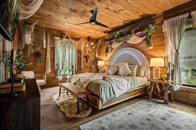 Primary suite with a backlit arched headboard, hanging greenery, and forest outside every window. Sleeping here becomes a story guests retell.