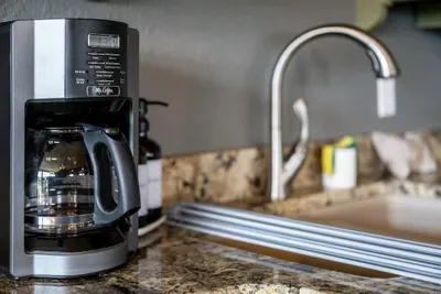 Coffee maker filled and a deep stainless sink beside it