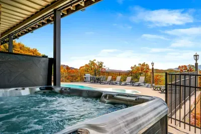 Bubbling hot tub steps from a private pool, with loungers, a grill, and outdoor dining framed by fall color and mountain views. Soak, swim, repeat — vacation mode: on.