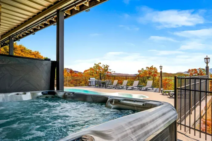 Bubbling hot tub steps from a private pool, with loungers, a grill, and outdoor dining framed by fall color and mountain views. Soak, swim, repeat — vacation mode: on.