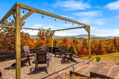 Mountain-view fire pit under glowing string lights, ringed by Adirondack chairs and fall color. S’mores by night, sweeping ridgeline views by day — the spot guests never want to leave.