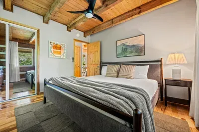 A handsome king bed anchors this airy bedroom — a soft throw, bedside lamps glowing low, and room to breathe under a slow-turning fan. The kind of room that makes you sleep in.