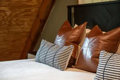 Leather accent pillows and crisp striped linens layered on a generous bed — the textured, dialed-in details that make this room an easy favorite. Sink in and stay put.