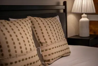 Layered linens and plush pillows on a solid wood frame — the details that turn a guest room into the one everybody quietly hopes to claim. Rest easy, sleep deep.