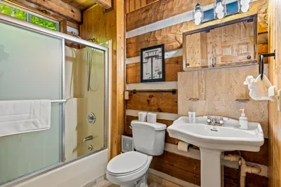 A log-walled bathroom with a glass shower, pedestal sink, and framed prints — compact, character-filled, and ready whenever you are. Cabin charm right down to the wash-up.