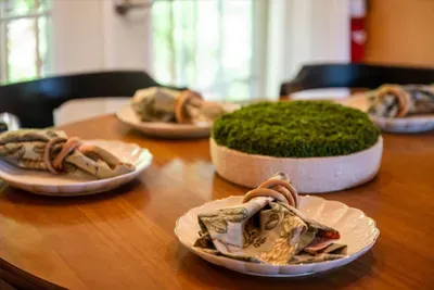 Little touches set the scene — rolled napkins, a moss centerpiece, and a wood table ready for the first shared meal. The kind of welcome that says the trip has already started.