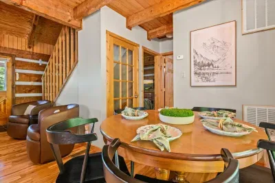 The dining table set and waiting beneath log-beam walls — room to seat the whole group for hearty breakfasts and lingering dinners. The shared meals are half the reason guests rebook.