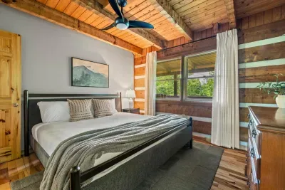 A welcoming bedroom framed in honey-toned log walls, layered bedding, and windows that pull the forest right in. Draw the curtains back and let the morning light wake you gently.
