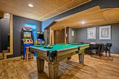 Pool table, arcade cabinet, and bar stools all under one roof — the game room built for tournament nights and friendly grudge matches. Step down and let the games begin.