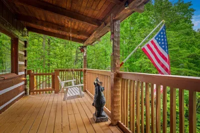 Old Glory snapping over a covered porch, a quiet bench, and trees in every direction — the kind of front-row seat to the forest that makes you cancel your plans. Stay put a while.