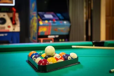 Balls racked and ready on the felt — break, sink, repeat, with arcade games glowing just over your shoulder. The opening shot of many late, laughter-filled nights.