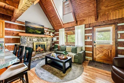 Gather around the wood-burning fireplace in this cathedral-ceiling living room — log walls, warm light, and an evening that slows all the way down.