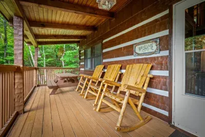 Cedar-log rockers wait beneath a covered porch, a welcome sign at the door and forest filling every gap in the rail. Rock, sip, repeat — the simplest part of the trip and the best.