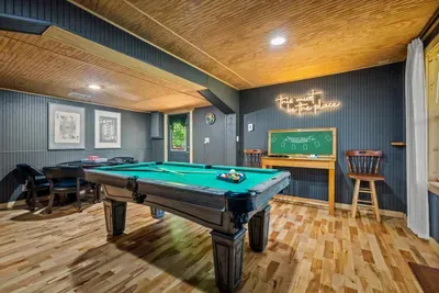 The game room glows after dark — a full-size pool table, chalkboard scorekeeping, and that neon sign setting the mood. Rack 'em up; this is where the night really gets going.