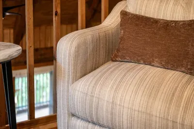 A plush upholstered armchair tucked by the window — the quiet corner for a morning coffee or the last chapter before bed. Every good cabin needs a chair like this.