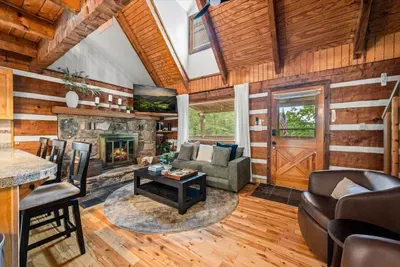 Vaulted log walls, a stone fireplace, and a leather chair angled toward the flames — this great room invites you to drop your bags and exhale. Mountain art and morning light included.