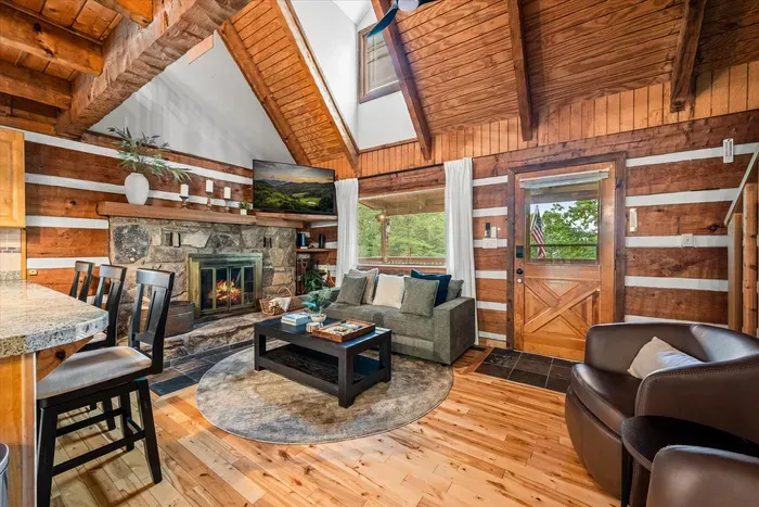 Vaulted log walls, a stone fireplace, and a leather chair angled toward the flames — this great room invites you to drop your bags and exhale. Mountain art and morning light included.