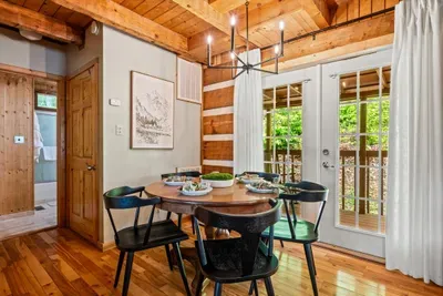 A round dining table sits under a chandelier with French doors opening to the deck — pass the plates, swap the day's stories, and let dinner stretch long. Where everyone gathers each night.