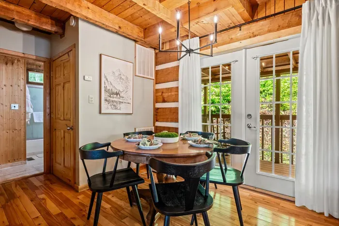 A round dining table sits under a chandelier with French doors opening to the deck — pass the plates, swap the day's stories, and let dinner stretch long. Where everyone gathers each night.