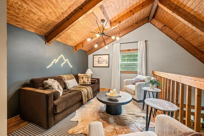 A loft lounge under vaulted wood ceilings, a starburst chandelier, and a glowing mountain-light wall — laid-back seating with a designer edge. Where the night winds down in style.