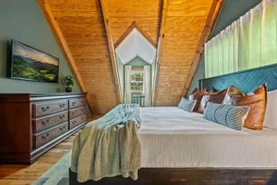 Tucked under the A-frame eaves with a smart TV, a roomy dresser, and leather-trimmed bedding — a private upstairs hideaway made for sleeping in. The peak-ceiling room with character.