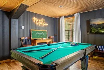 Sun spills across the felt while the neon hums — pool table, chalkboard, and room to roam make this the heart of the cabin after dark. Where every trip earns a rematch.